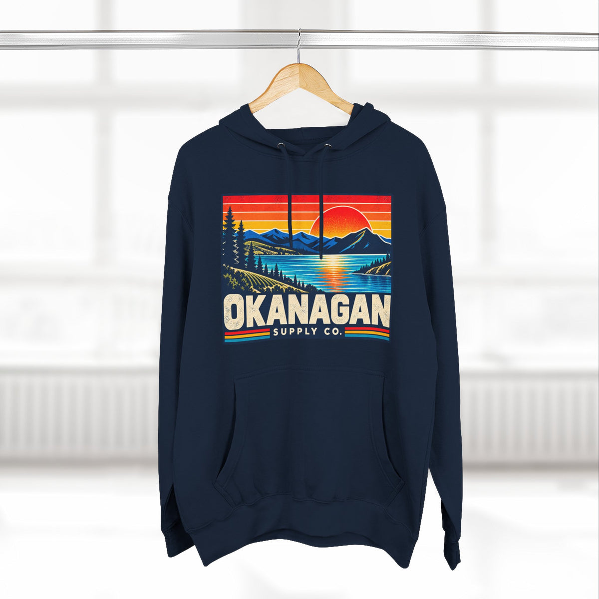 Okanagan Supply Co. Retro Sunset Hoodie in navy, hanging on a rack