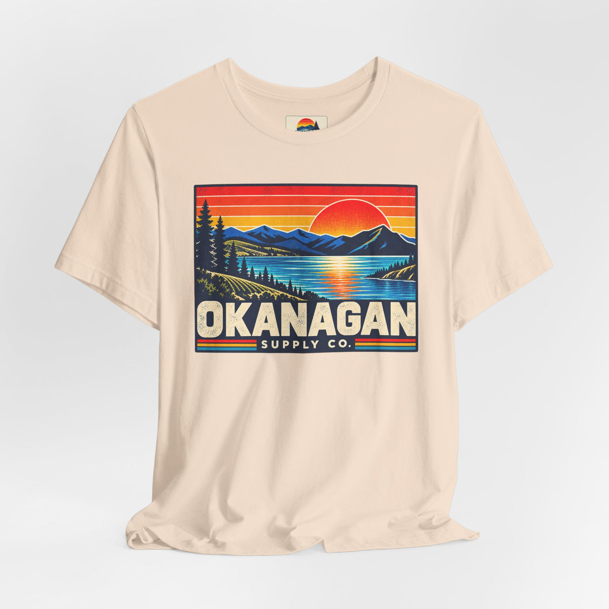 Okanagan Supply Co. Retro Sunset Tee in soft cream, styled flat view with sunset badge