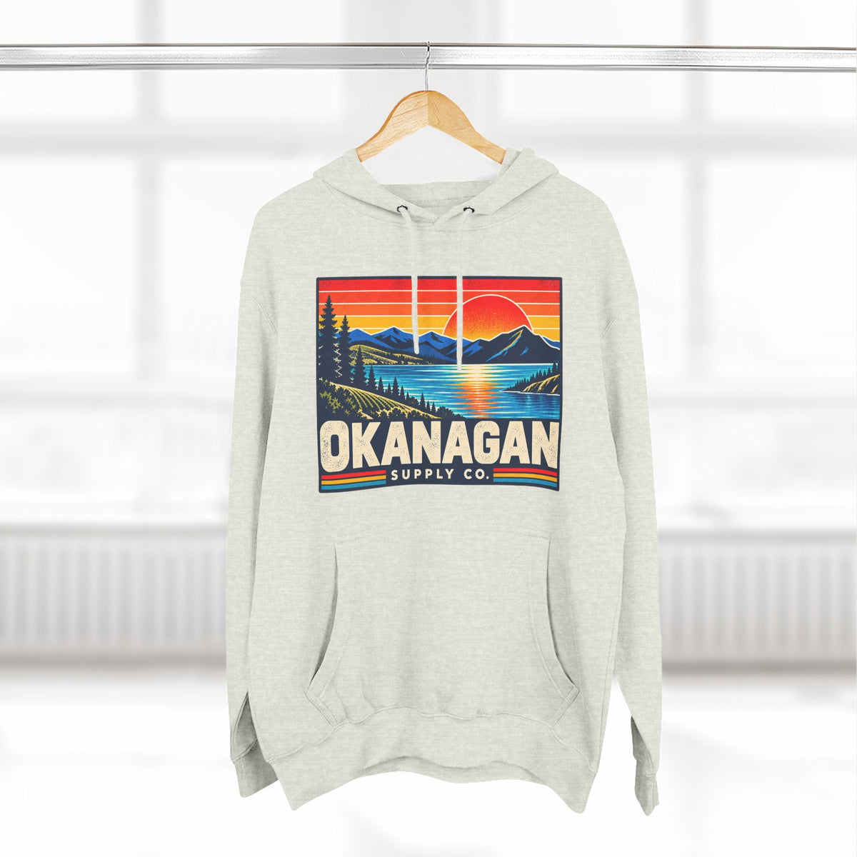Okanagan Supply Co. Retro Sunset Hoodie in oatmeal heather, hanging on a rack