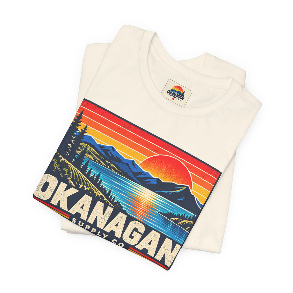 Okanagan Supply Co. Retro Sunset Tee in natural, folded to show the sunset badge print and inside collar label