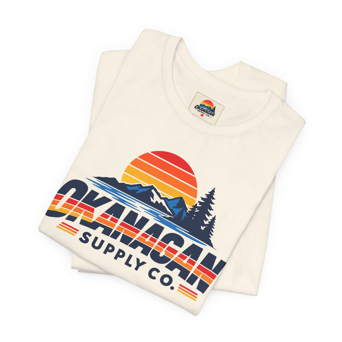 Okanagan Supply Co. Vintage Outdoors Tee in natural, folded to show the retro sunset, mountain and pine print and inside collar label