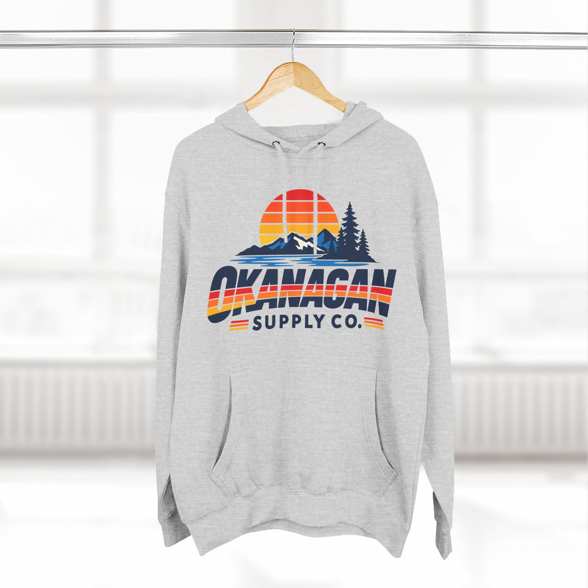 Okanagan Supply Co. Vintage Outdoors Hoodie in heather grey, hanging on a rack