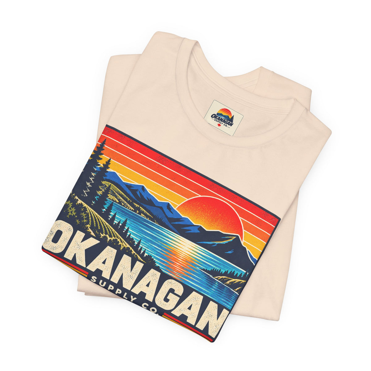 Okanagan Supply Co. Retro Sunset Tee in soft cream, folded to show the sunset badge print and inside collar label