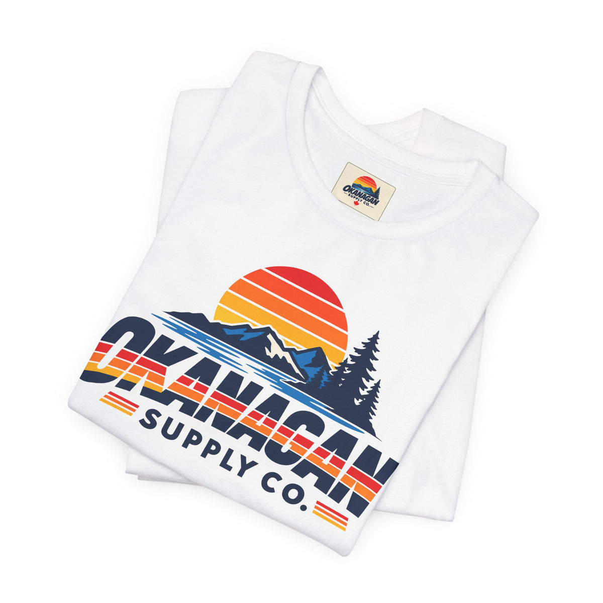 Okanagan Supply Co. Vintage Outdoors Tee in white, folded to show the retro sunset, mountain and pine print and inside collar label