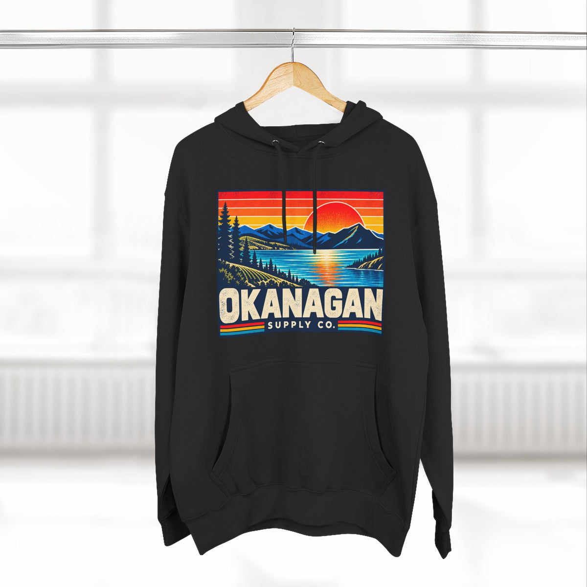 Okanagan Supply Co. Retro Sunset Hoodie in black, hanging on a rack