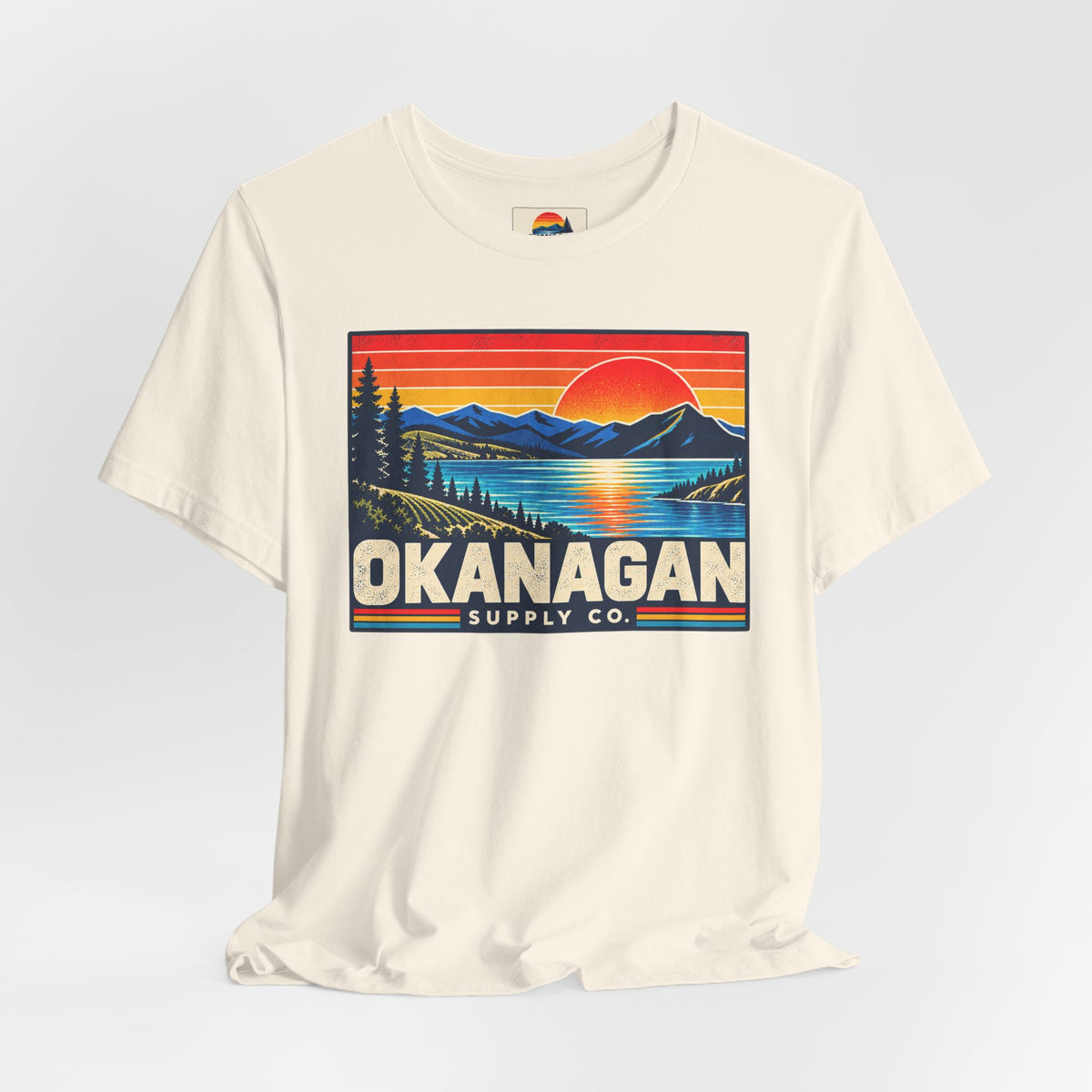Okanagan Supply Co. Retro Sunset Tee in natural, styled flat view with sunset badge