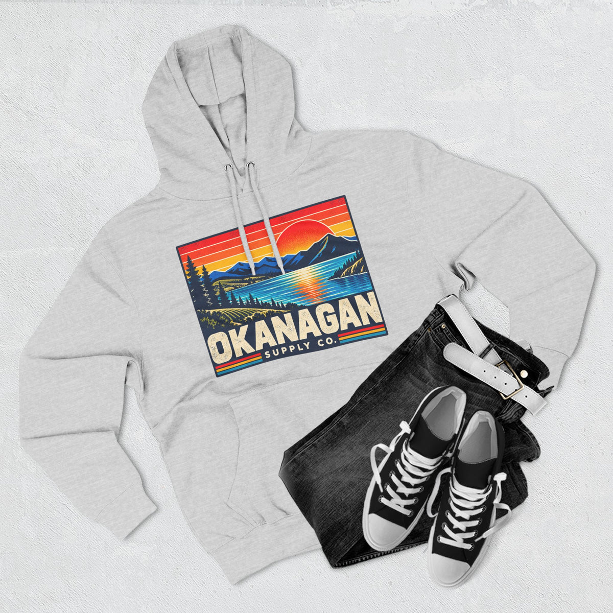Okanagan Supply Co. Retro Sunset Hoodie in heather grey, flat lay with jeans and sneakers